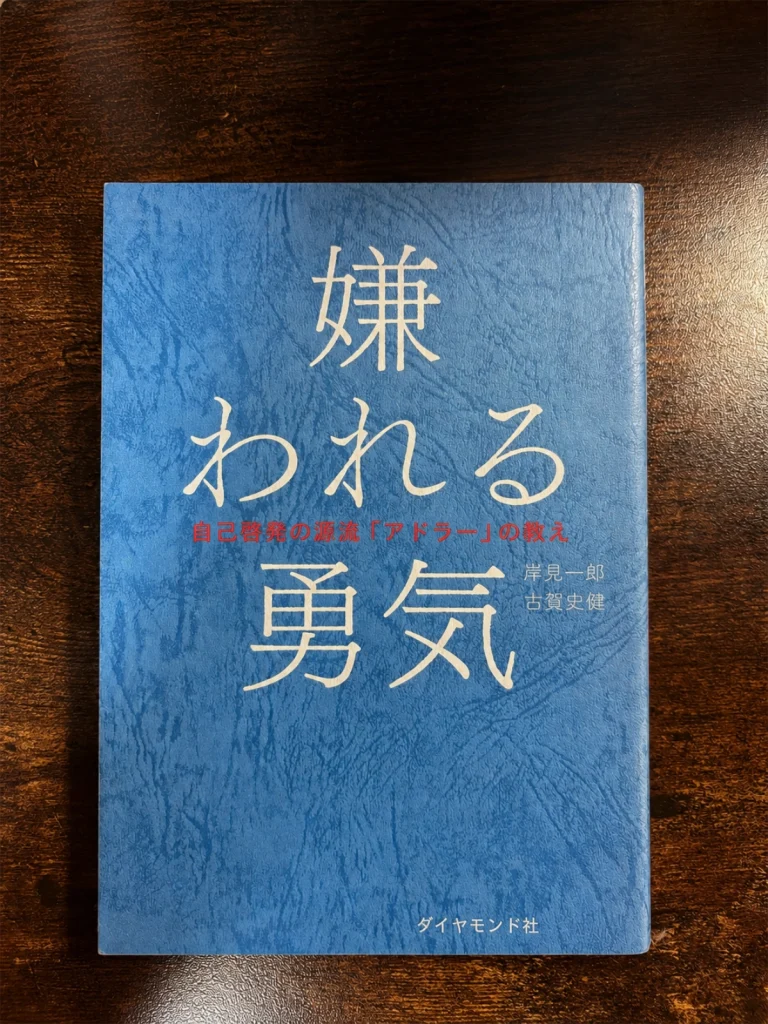 岸見一郎・古賀史健著『嫌われる勇気』の本を木目の上に置いて撮影した写真