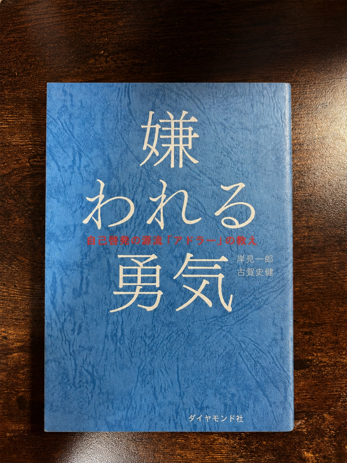 岸見一郎・古賀史健著『嫌われる勇気』の本を木目の上に置いて撮影した写真