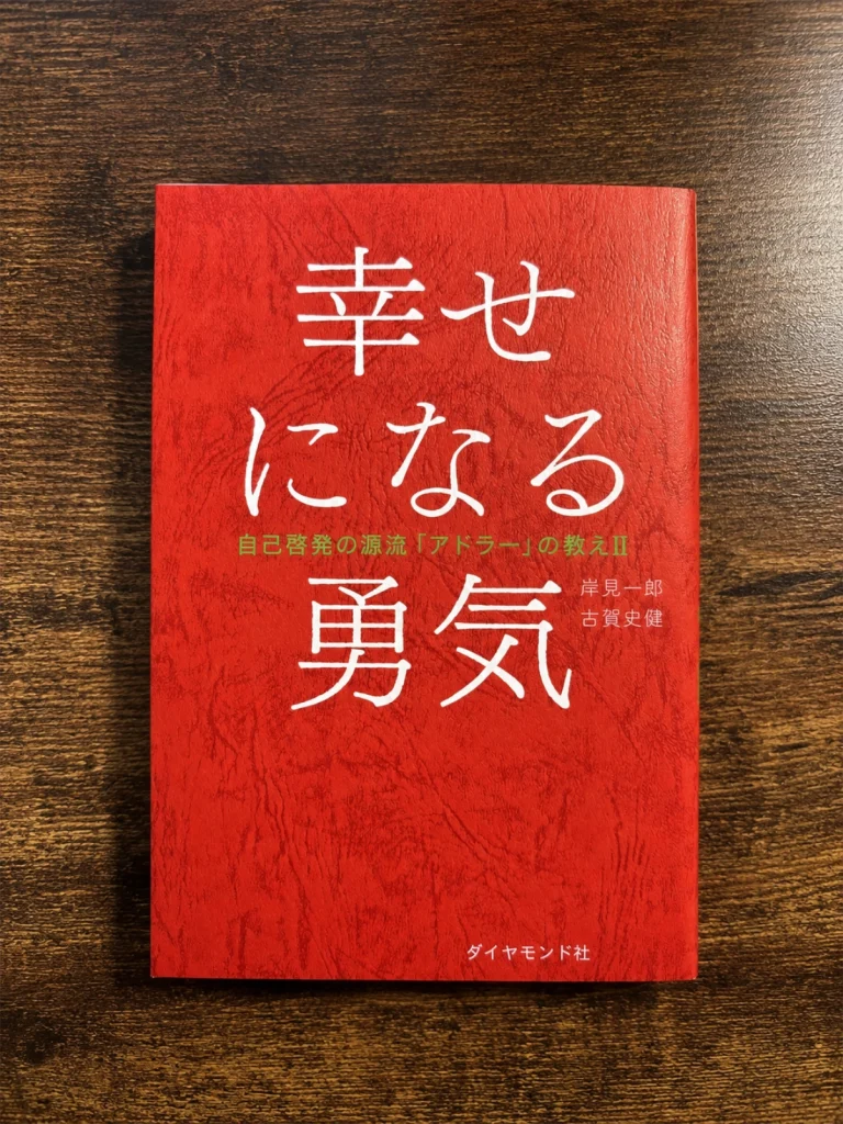 岸見一郎・古賀史健著『幸せになる勇気』の本を木目の上に置いて撮影した写真
