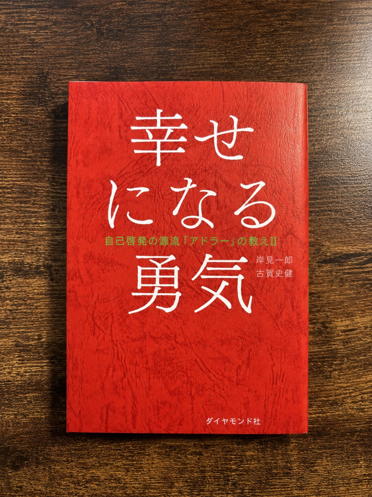 岸見一郎・古賀史健著『幸せになる勇気』の本を木目の上に置いて撮影した写真